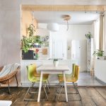 zrekonštruovaný starý svetlý byt so smrekovou podlahou, prúteným kreslom, stojacou lampou, jedálenským stolom a farebnými stoličkami, a s kuchyňou, ktorá je priestorovo oddelená skrinkami