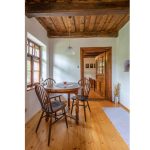 Interiér zrekonštruovanej tradičnej chalupy s masívnym dreveným stropom, okrúhlym starodávnym jedálenským stolom a stoličkami.