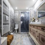 Vintage kúpeľňa so sprchovacím kútom, zrecyklovaným príborníkom, košom na bielizeň a obkladom s patchworkovým vzorom.
