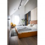 Spálňa s koženou posteľou v hnedej farbe a bielosivým posteľným prádlom, so žltým kreslom a posuvnými dverami v čiernej farbe