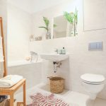 Neutrálne pôsobiaca kúpeľňa s bielym obkladom, vaňou, umývadlom, WC, dreveným stojanom na utierky a zvieracím motívom v podobe zebrovaného koberčeka