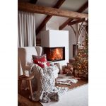 Vianočná obývačka s ušiakom s merino pletenou dekou a vankúšom so sobom, stromčekom s darčekmi a horiacim kozubom.