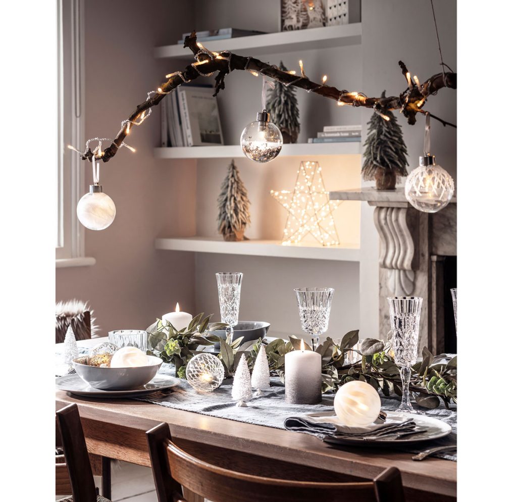 Menej tradičná vianočná výzdoba: vetva so svetielkami zavesená nad sviatočným stolom