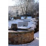 zimná atmosféra v storočnej záhrade: kamenná kruhová fontána od ktorej vedú schody k liatinovej pumpe na vodu