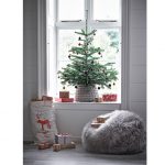 Vianočný stromček v pletenom koši umiestnený v okennom výklenku, pod ním je kožušinový vak na sedenie a vrece na darčeky
