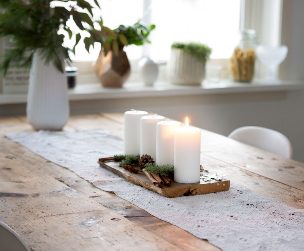 Adventná dekorácia: drevená doska s bielymi sviečkami, vetvičkami, škoricou a šiškami