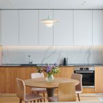 kuchyňa s jedálňou: kuchynská minimalistická stena, ktorá ukrýva potraviny a spotrebiče, s osvetlenou linkou a náladovým podsvietením záclon