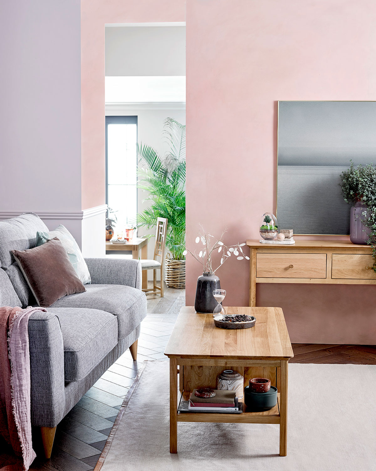 obývačka so sivou sedačkou, dreveným stolíkom, pastelovými vankúšmi a pastelovou stenou