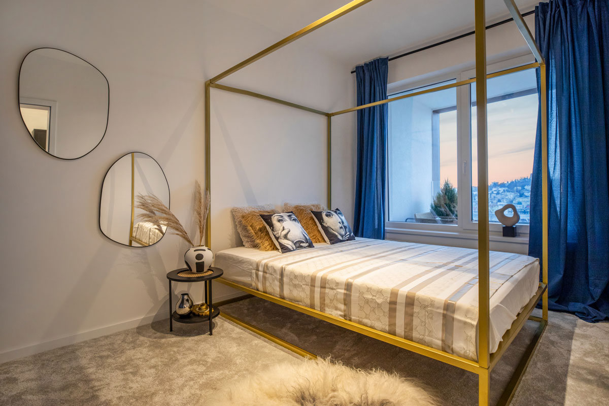 extravagantná spálňa so zlatou posteľou, zrkadlami nepravidelného oválneho tvaru a modrými závesmi