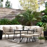 Záhradná obývačková terasa s bielou sedačkou, tropickými rastlinami a latkovým oplotením