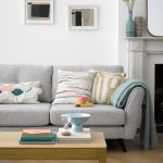 obývačka v pastelových farbách, so sivou sedačkou, vankúšmi a jednoduchým dreveným stolíkom