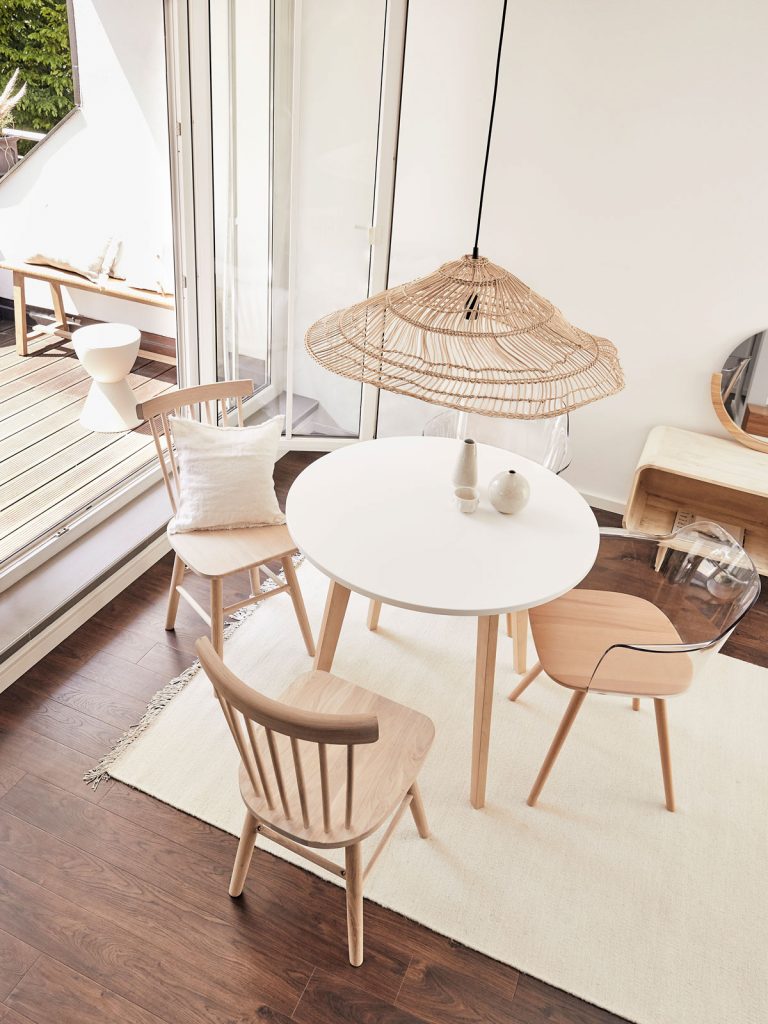 Jednoduchý jedálenský kút so stolom a stoličkami oživený ratanovým tienidlom na lustri