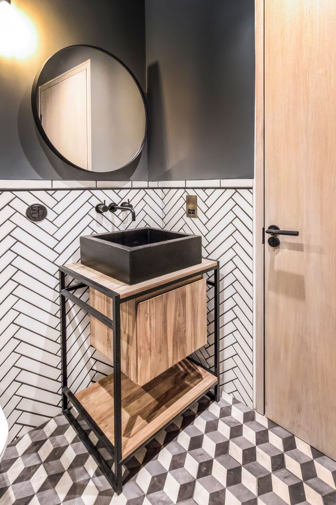 menšia kúpeľňa v industriálnom štýle v kombinácii hnedej a čiernej farby, s obkladom vzoru rybej kosti a podlahou s 3D efektom kociek