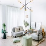 obývačka so sivými kreslami, zelenou taburetkou, prírodným kobercom, skrinkou, čiernym stolíkom s dekoráciami a viacramenným lustrom v čierno-zlatej kombinácii