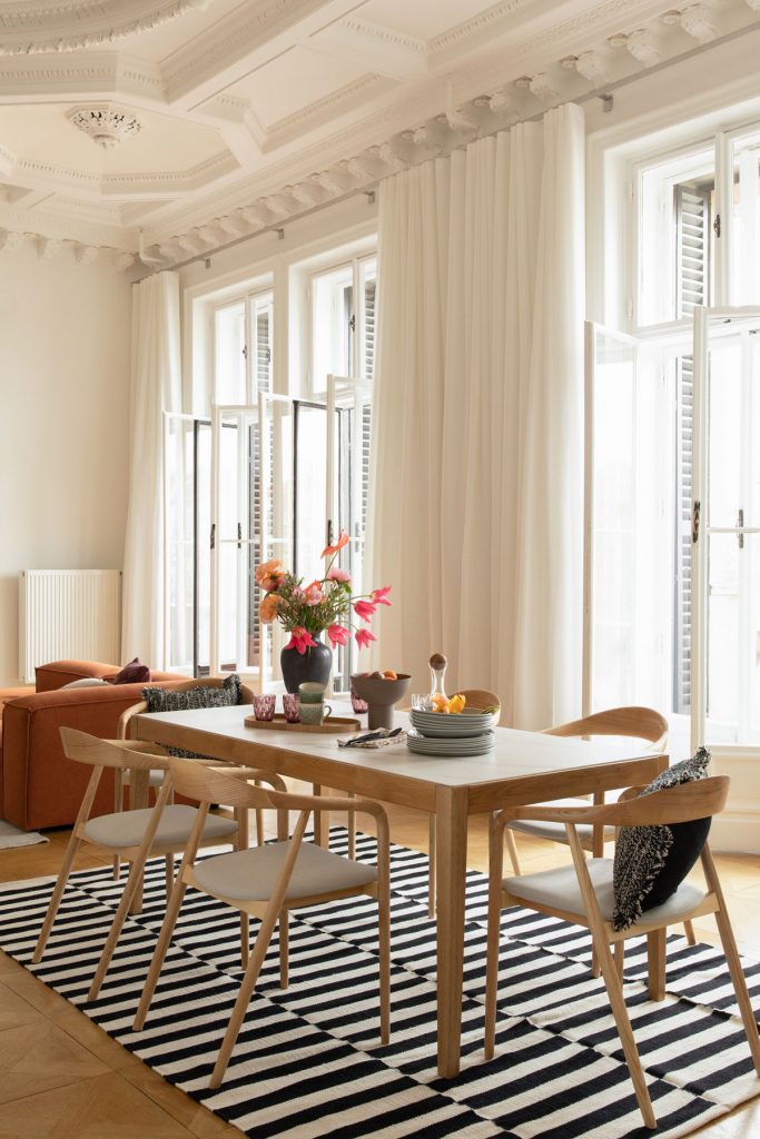 Jedáleň spojená s obývačkou, drevený stôl a dizajnové drevené stoličky, pásikavý čierno-biely koberec