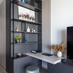 detail obývačky so sivou otvorenou skriňou, TV poličkou a pracovným kútikom vytvoreným z dosky a taburetky