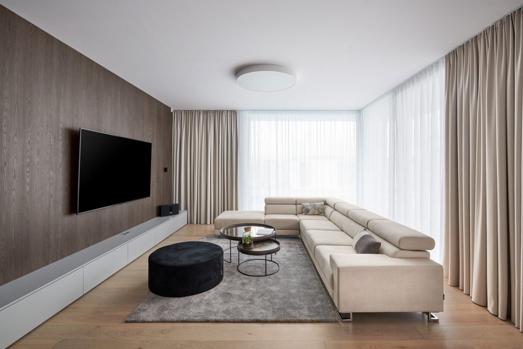 moderná minimalistická obývačka s béžovou rohovou sedačkou, okrúhlymi konferenčnými stolíkmi, taburetom, sivým kobercom a TV stenou