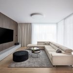 moderná minimalistická obývačka s béžovou rohovou sedačkou, okrúhlymi konferenčnými stolíkmi, taburetom, sivým kobercom a TV stenou