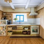 kuchyňa na chalupe s jednoduchou kuchynskou otvorenou linkou, dreveným obkladom na stene a zelenými zárubňami a dverami