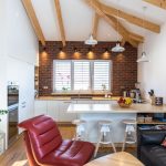 otvorený priestor obývačky a kuchyne s bielou kuchynskou linkou, tehlovou stenou, polostrovčekom, čiernou sedačkou a červeným kreslom