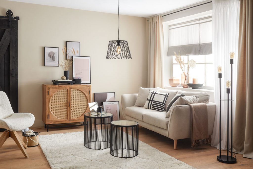 Obývačka so svetlou sedačkou, smotanovým kobercom, kovovými stolíkmi a drevenou skrinkou s vypletanými dvierkami