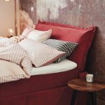 spálňa s červenou čalúnenou posteľou a tapetou s ošúchaným vzhľadom steny