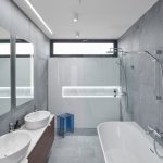 minimalistická kúpeľňa s vaňou, dvoma umývadlami, sprchovacím kútom a stenou s podsvieteným výklenkom