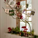 Sviatočné zátišie na parapete so sklenenou vázou s konárom, na ktorom sú povešané vianočné pohľadnice, vedľa vázy je dekorácia z muchotrávok