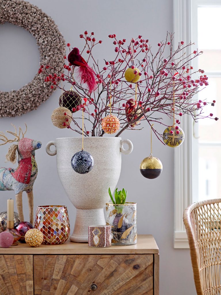 keramická dizajnová váza s vetvičkami, na ktorých visia farebné vianočné ozdoby
