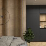Detail steny v drevodekóre s minimalistickými industriálnymi hodinami, sivou sedačkou a čiernou kuchyňou