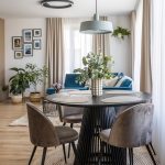 interiér zariadený v štýle cozy living, s jedálenským okrúhlym stolom a elegantnými čalúnenými stoličkami, s pleteným prírodným kobercom a modrou sedačkou