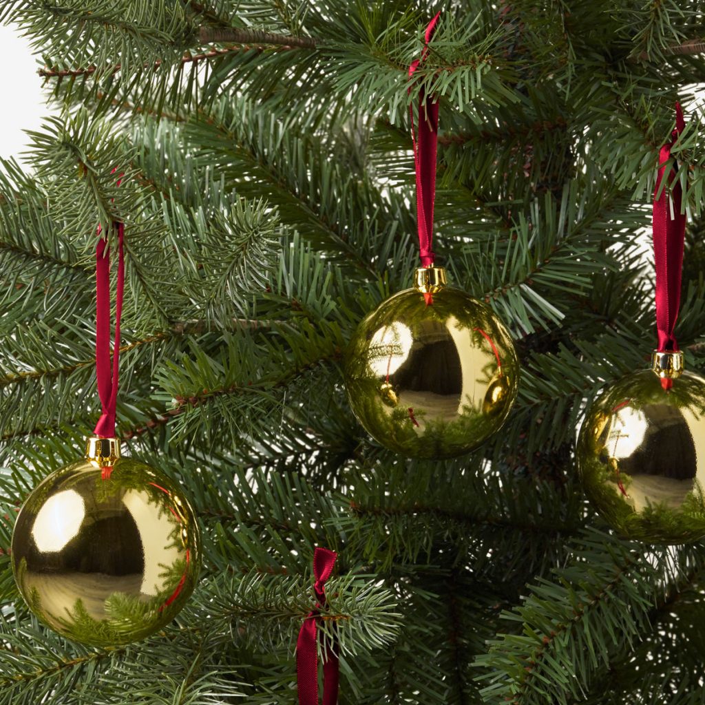 Vianočné zlaté gule zavesené na stromčeku na červených stužkách