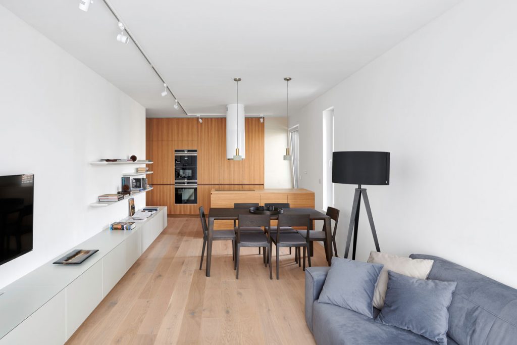 Otvorený priestor obývačky, jedálne a kuchyne so závesnými skrinkami, jedálenským stolom, sedačkou a kuchyňou v drevodekore