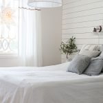 škandinávska spálňa s bielym dreveným obkladom na stene, textíliami na posteli v sivej a bielej, vianočnou ozdobou v podobe stromčeka, bieleho svietnika a hviezdy