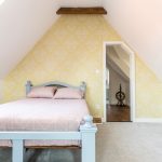 Podkrovná spálňa s pastelovo modrou posteľou a žlto-bielou vzorovanou maľovkou