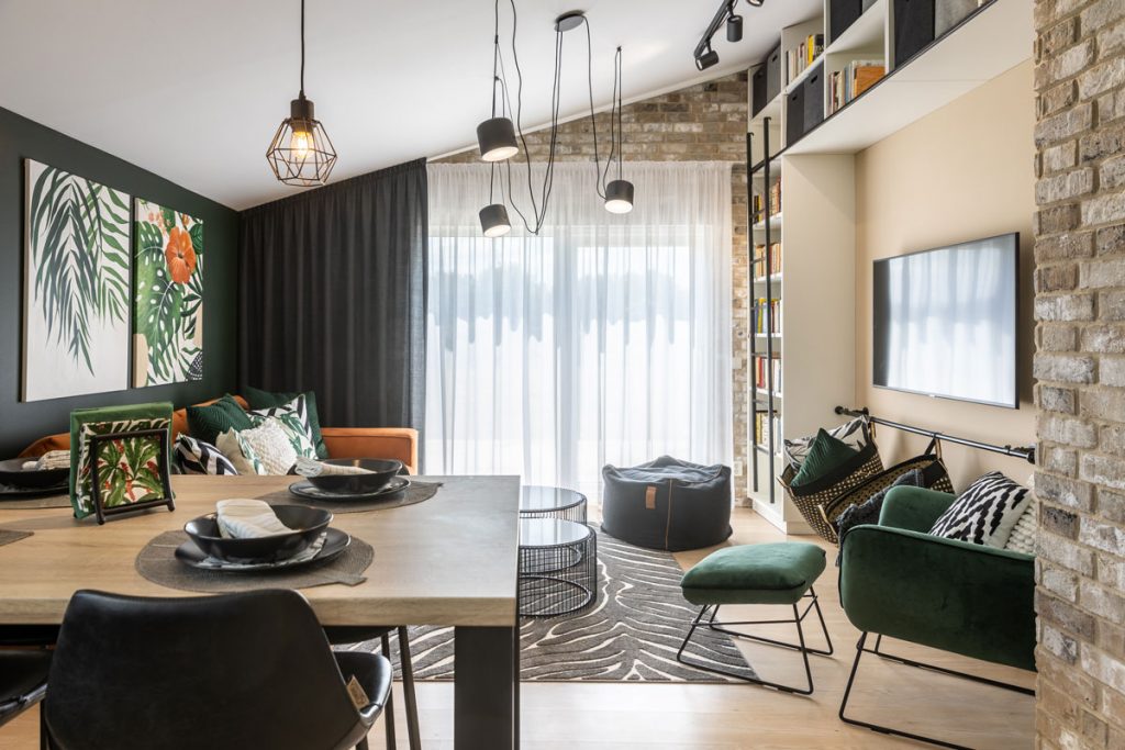 Otvorený priestor obývačky a jedálne, zariadený vo farbách oranžovej, čiernej a zelenej, s prírodnými a zamatovými prvkami