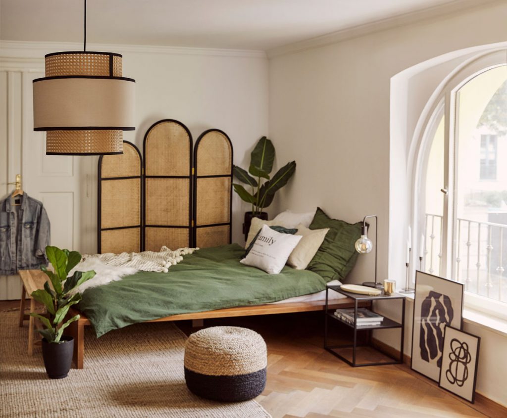 Interiér v prírodnom štýle s jednoduchou drevenou posteľou a paravánom a svietidlom s viedenským výpletom