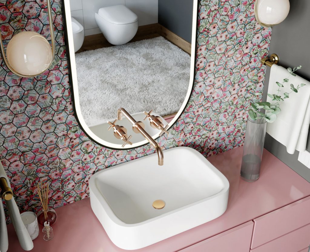 Kúpeľňa s pastelovo ružovou skrinkou, umývadlom, zlatými prvkami, oválnym zrkadlom a farebným obkladom