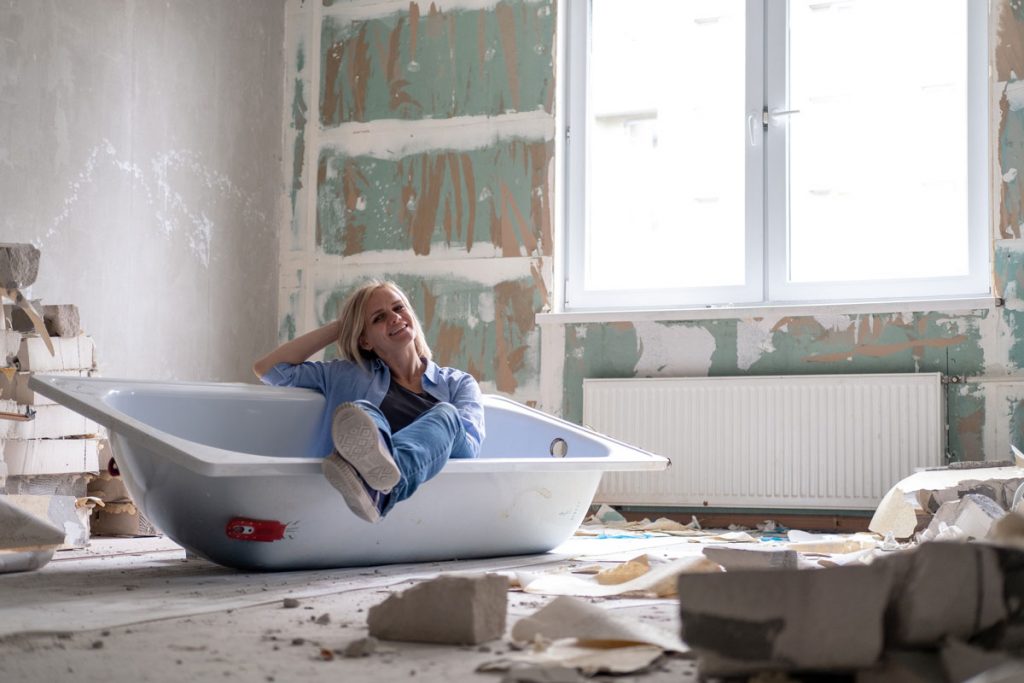 žena sediaca vo vani v miestnosti, kde prebieha rekonštrukcia