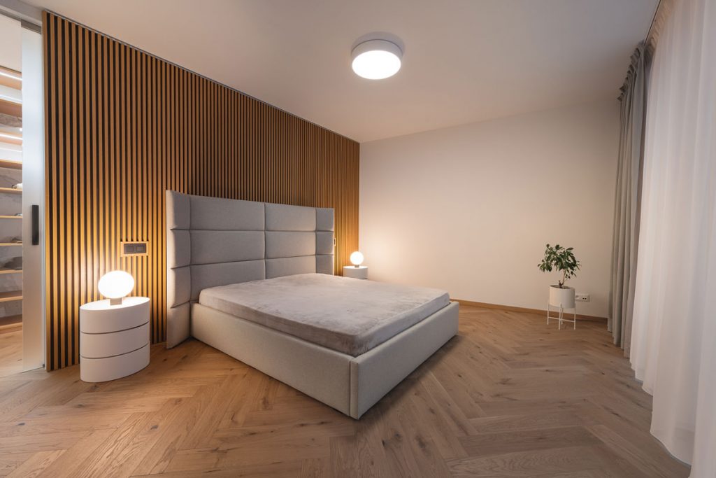Moderná minimalistická spálňa s lamelovým obkladom na stene a čalúnenou posteľou s čelom s ohnutými bokmi