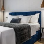 kontinentálna čalúnená posteľ v modrej farbe doplnená kontrastnými svietidlami spustenými zo stropu