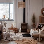 obývačka s drevenou etnou sedačkou, krémovou sedačkou, jutovými kobercami, textíliami v etno a vidieckom štýle, skrinkou s výpletom, pieckou a dreveným obkladom na stene