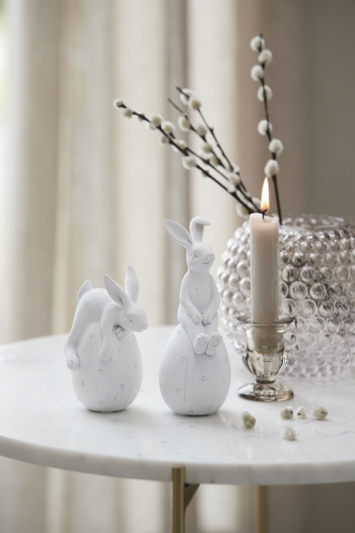 Jednoduchá veľkonočná dekorácia v podobe keramických zajačikov, sviečky a vázy s bahniatkami