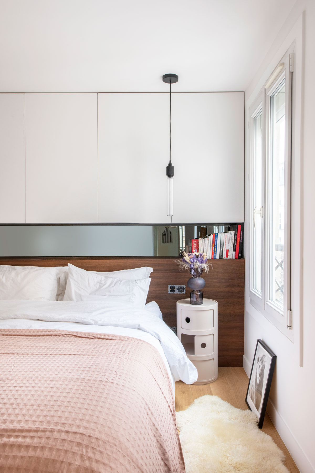 Spálňa v kombinácii bielej s orechom, s modernou zástenou, okrúhlym nočným stolíkom a kožušinou na podlahe