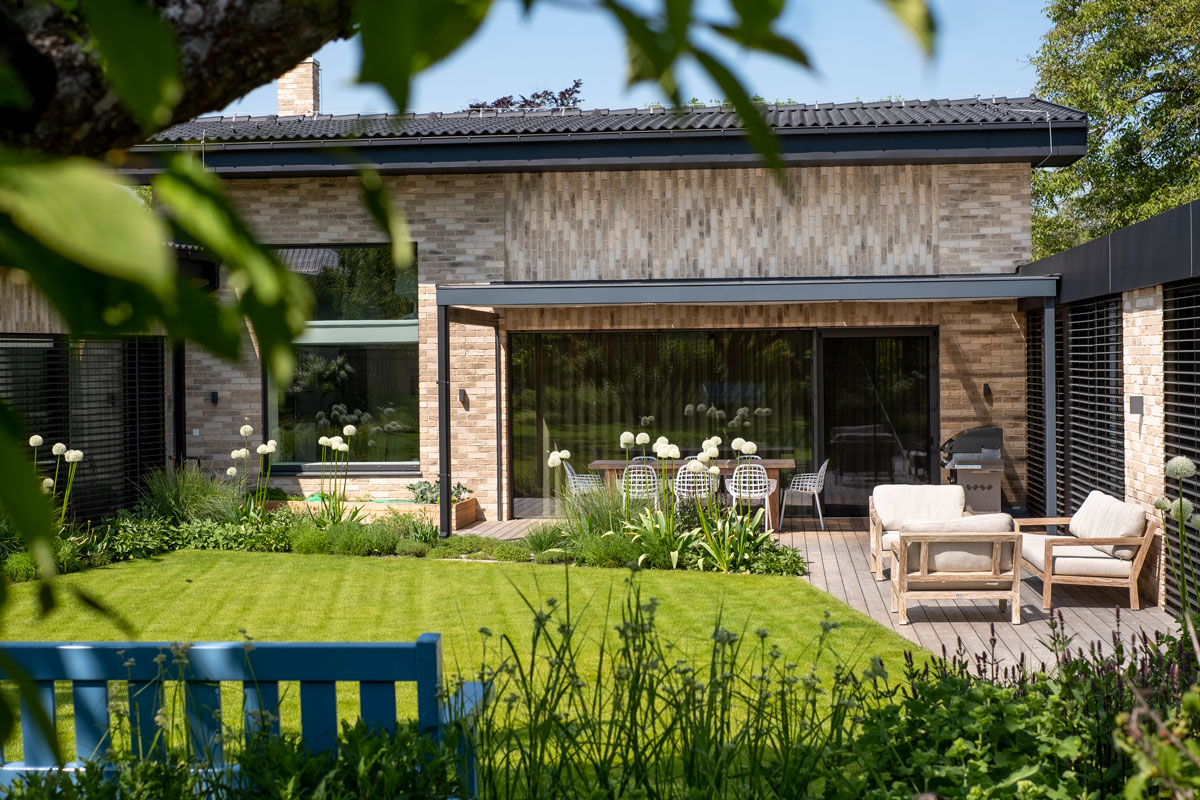 Moderný rodinný dom s čiastočne zastrešenou drevenou terasou s grilom a posedením, trávnikom a okrasnými záhonmi
