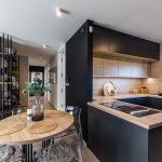 moderný interiér s otvoreným konceptom kuchyne a obývačky, kuchyňa má dubovú pracovnú dosku a skrinky a antracitový spodok s ostrovčekom, od obývačky ju oddeľuje antracitová tabuľová stena