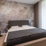 minimalistická spálňa so sivou čalúnenou posteľou, šatníkom, nemým sluhom a tapetou za posteľou s motívom mapy