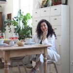 Sarah Tognetti, majiteľka domu vo svojej jedálni sedí za dreveným stolom, za ňou je biela vysoká skrinka so šuflíkmi, interiér bol zariadený v duchu udržateľnosti