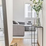 Chodba s jednoduchým kovovým stolíkom a pohľad do obývačky so sivou sedačkou