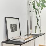 jednoduchý tmavý kovový stolík s vázou s kvetmi, sivými sviečkami, zarámovanou fotografiou a knihami
